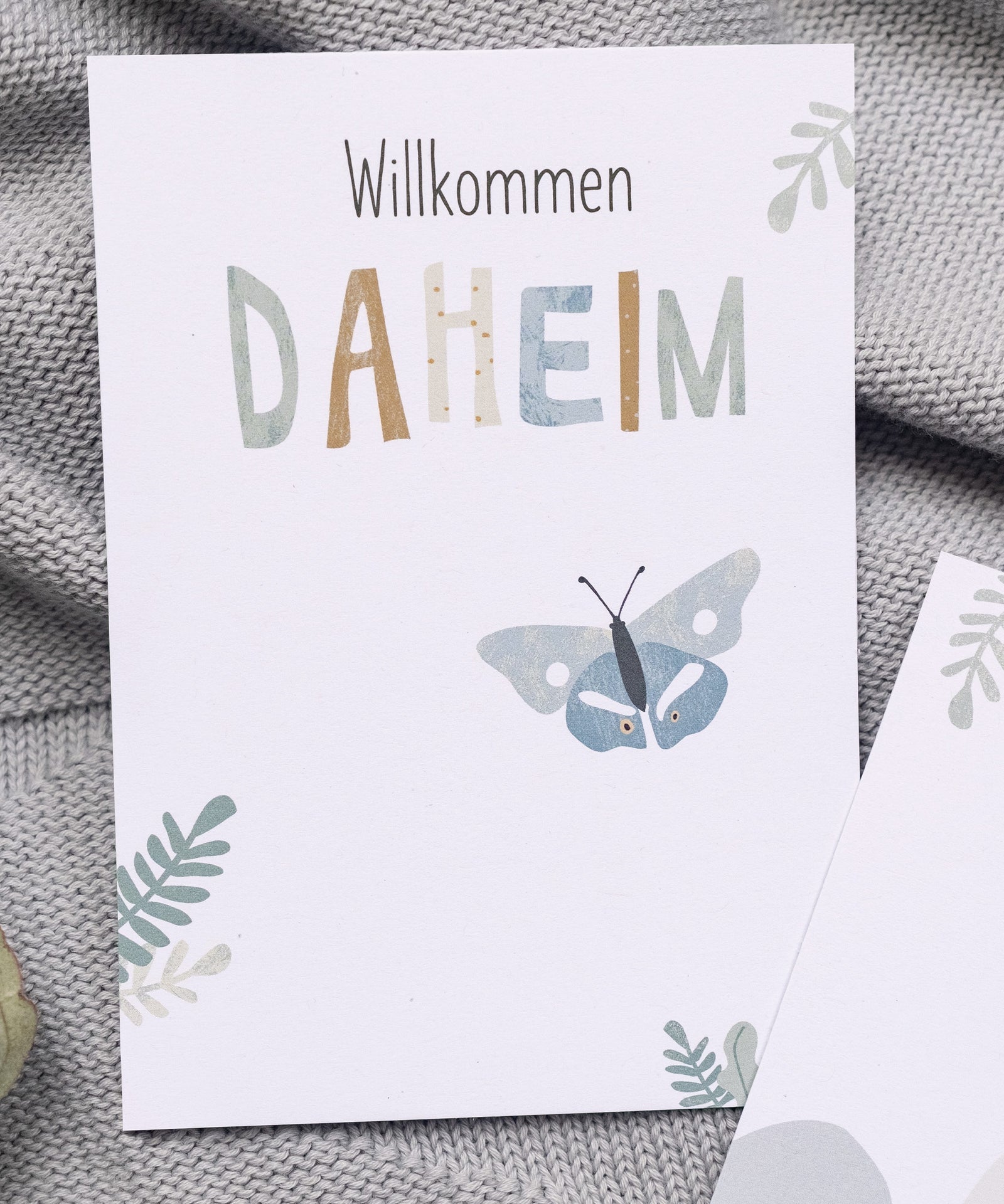 Meilensteinkarte mit Text "Willkommen daheim" und Schmetterling-Illustration.