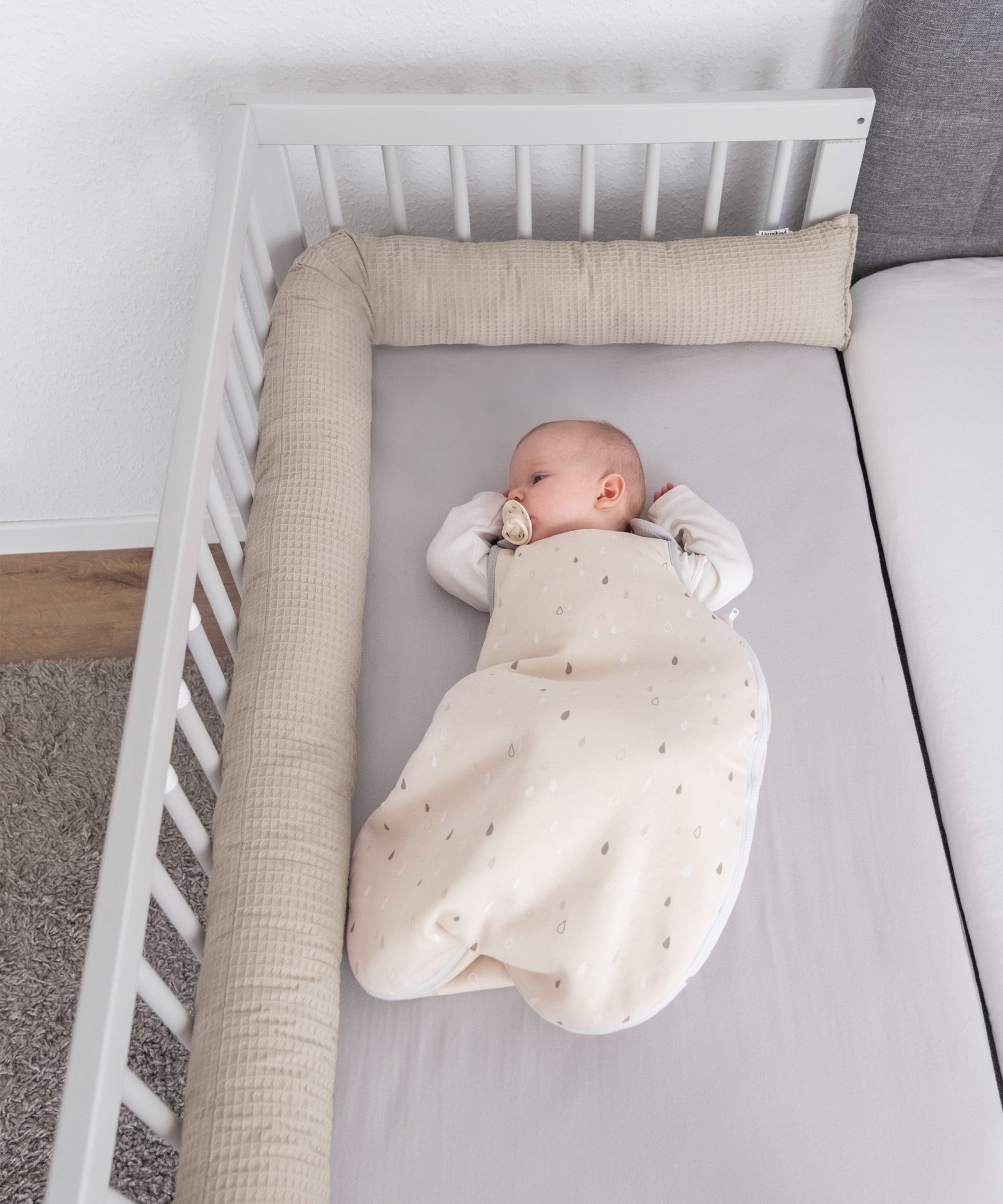 Baby liegt in Beistellbett mit der Bettschlange am Bettgitter entlang.