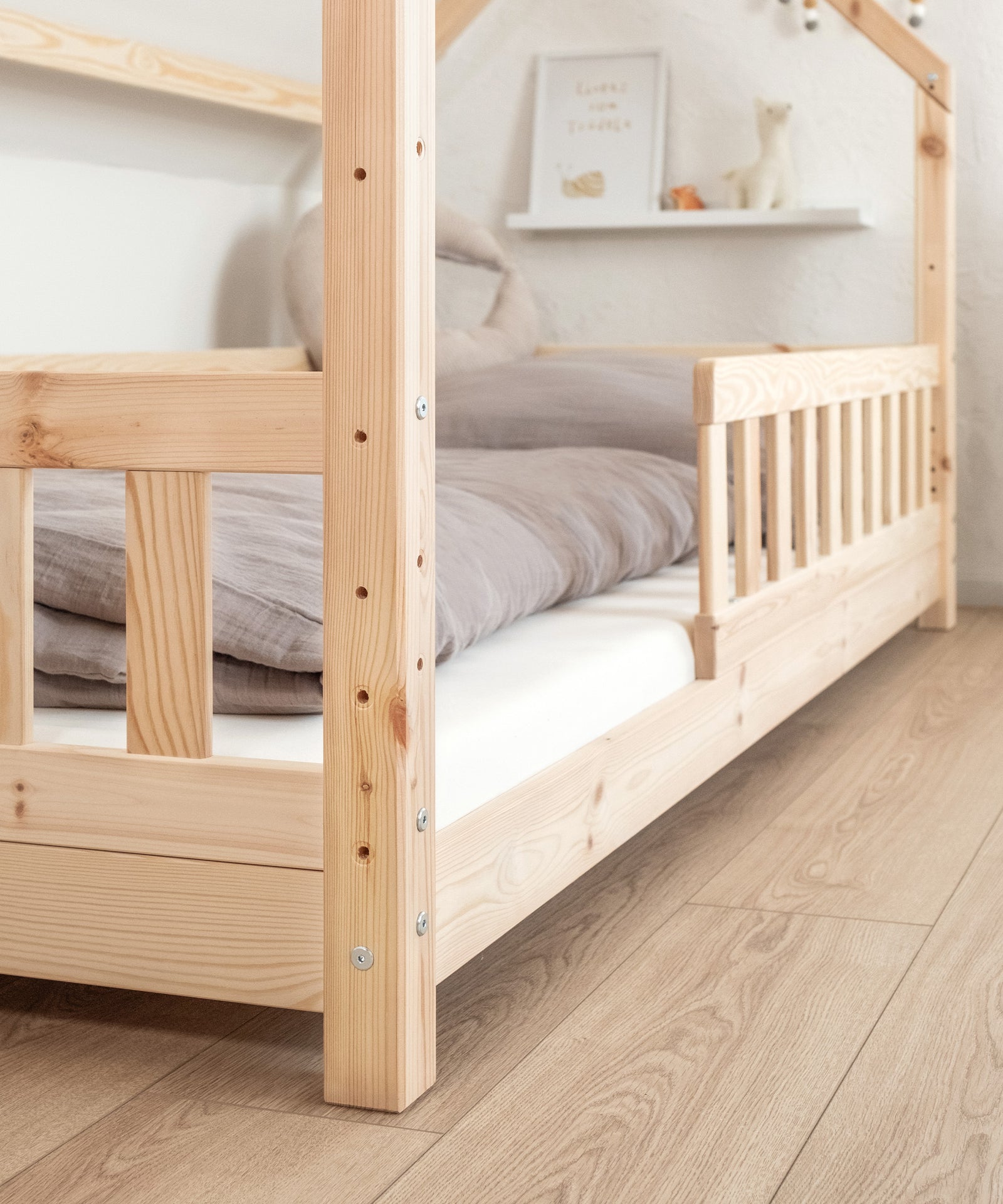 Höhenverstellbar*Dank vorgebohrter Löcher ergeben sich zwei Liegehöhen: Bodennah 9 cm oder 25 cm mit Platz für Bettkasten oder Schubladen.|Nahaufnahme Hausbett Kiefer Natur bodennah montiert.