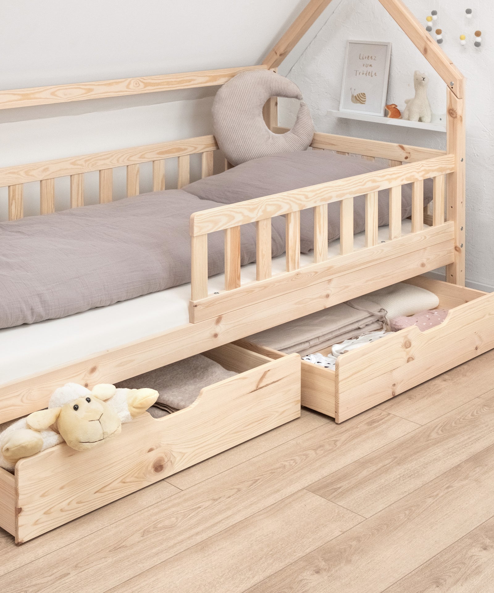 Extra Stauraum*Unsere optionalen Bettschubladen bieten zusätzlichen Stauraum für Groß und Klein.|Hausbett Kiefer Natur mit gefüllten, halb ausgezogener Doppelschublade.