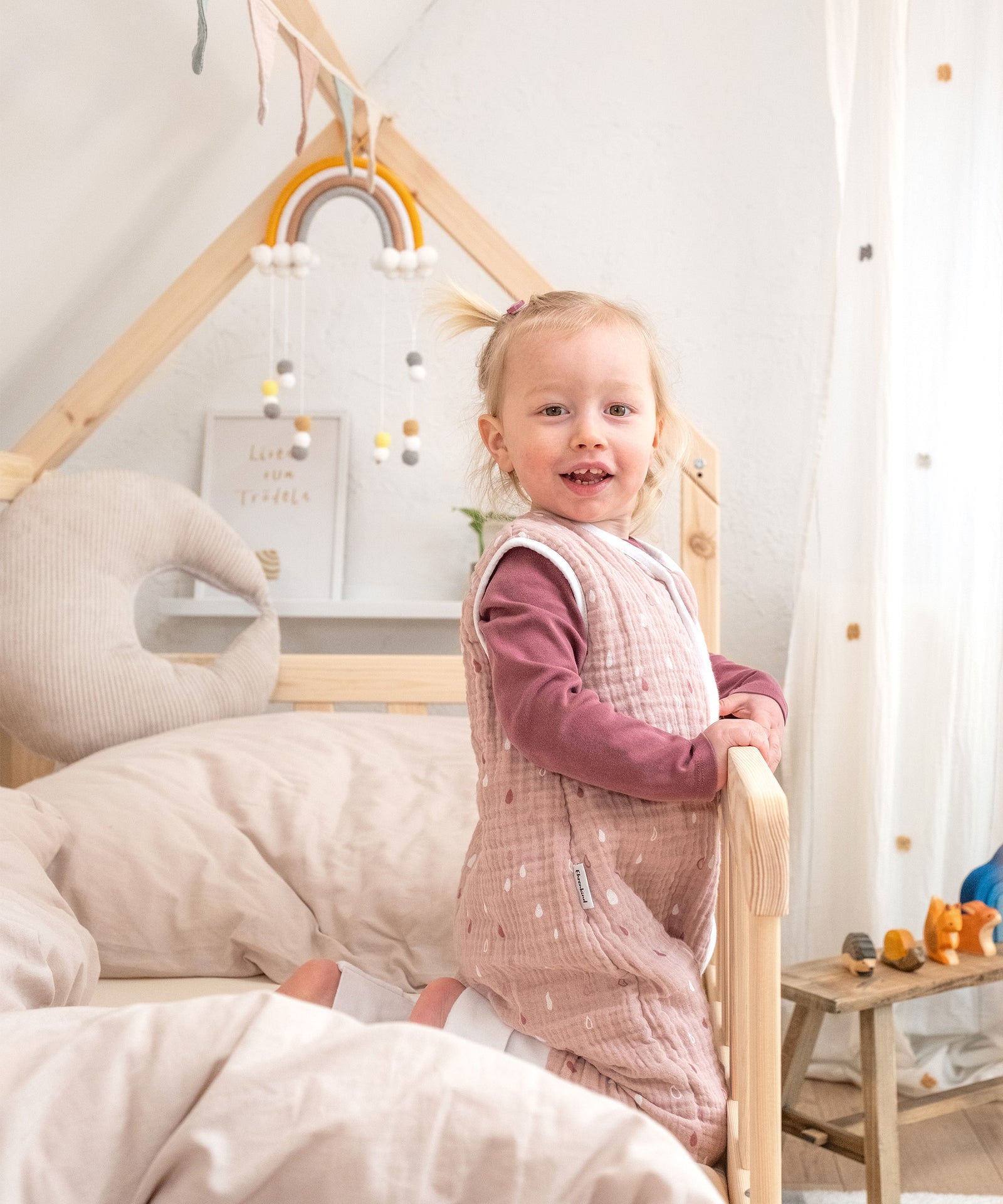 Mädchen in Hausbett Kiefer Natur sitzt neben Rausfallschutz.