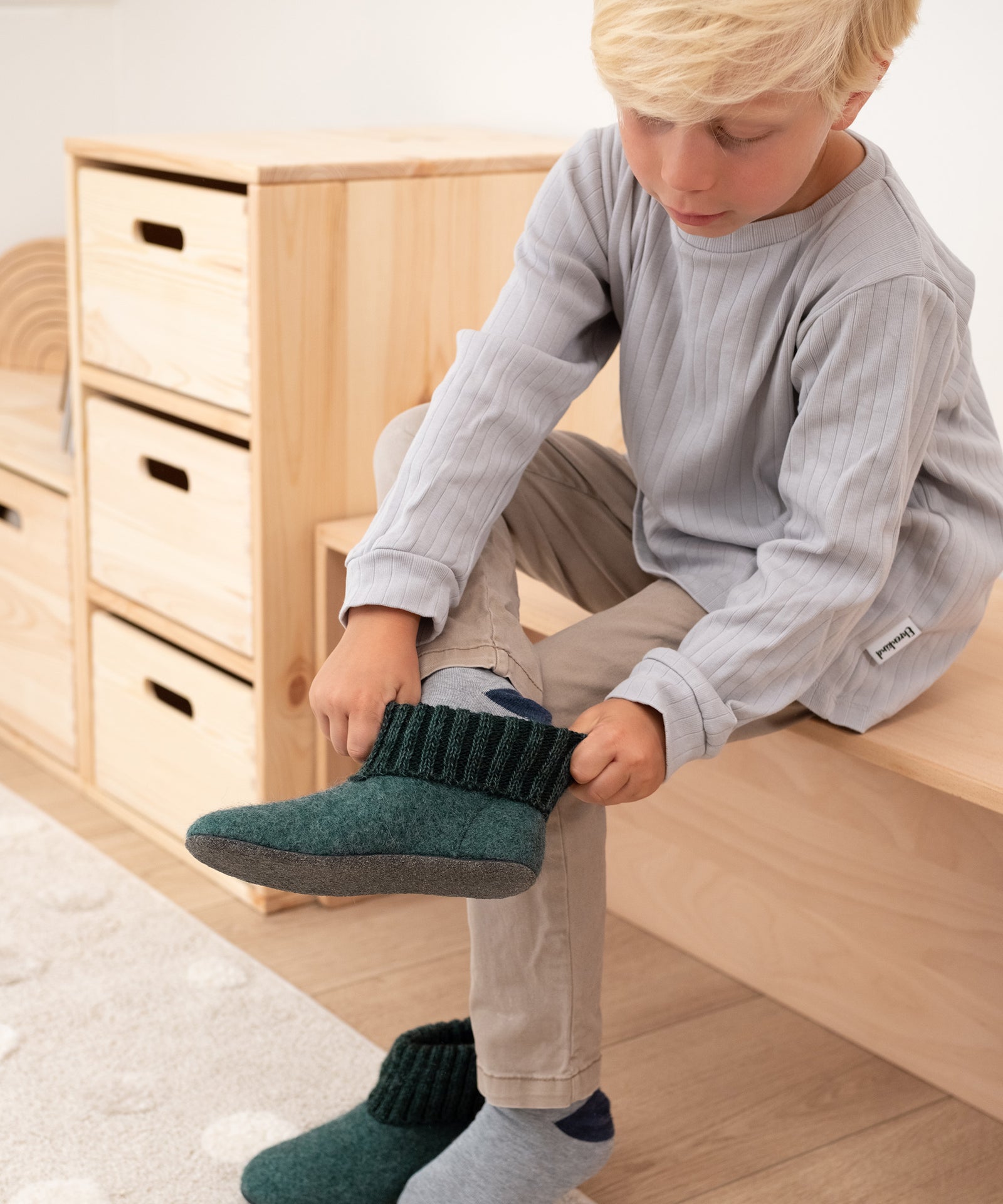 Elastischer Strickbund*Die weichen und elastischen Strickbündchen machen das Anziehen kinderleicht und bieten einen guten Halt.|Junge zieht Hüttenschuhe mit Strickbündchen in Waldgrün an.