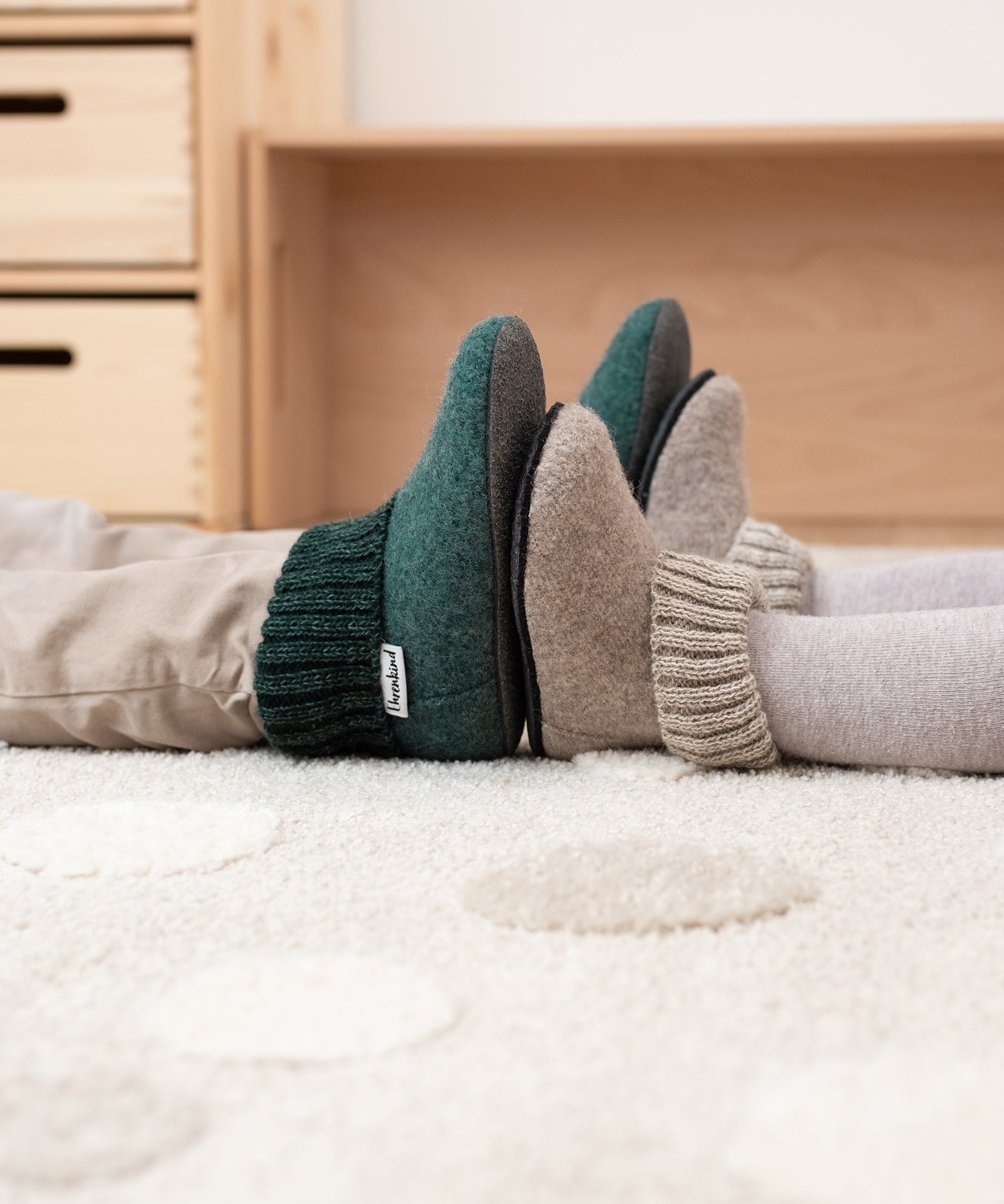 Perfekt für jede Fußform*Die hochwertigen Hüttenschuhe werden über Leisten gefertigt und passen sich jeder Fußform perfekt an. So bequem und gemütlich!|Zwei Kinder mit unterschiedlich großen Hausschuhen sitzen sich Fuß an Fuß gegenüber.