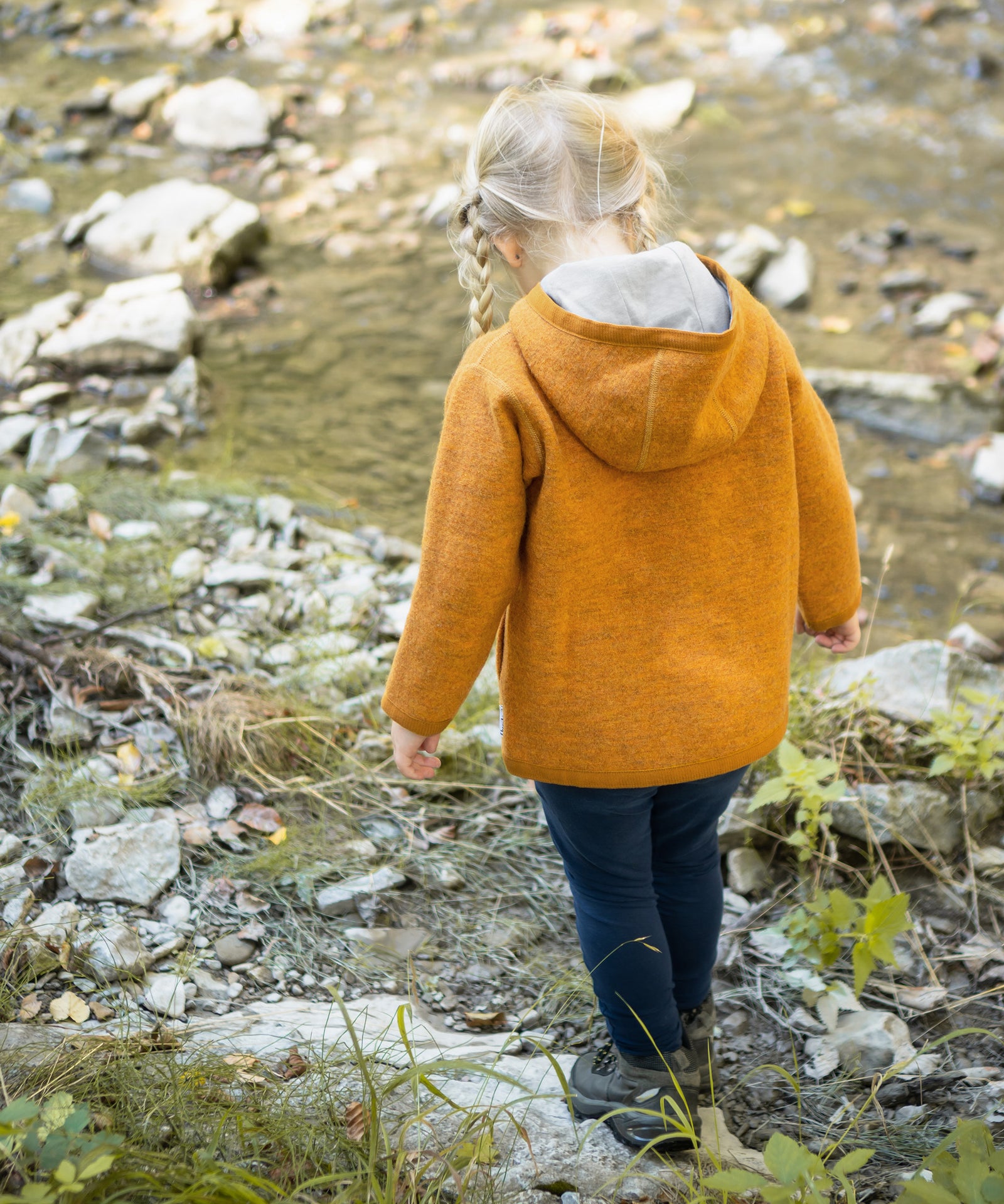 Kind mit Walkjacke in safrangelb am Bach.