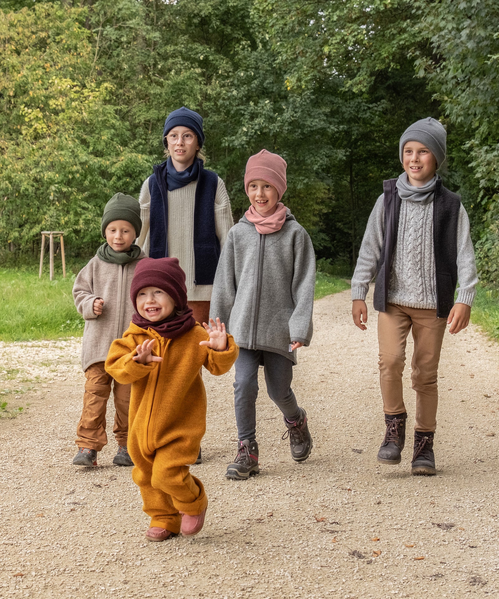 Eine Größe für alle*Der Rippstrick ist sehr dehnbar und der Umschlagbund lässt sich variabel aufschlagen. So passt die Mütze allen von ca. 2 bis 12 Jahren.|Fünf Kinder von klein bis groß laufen auf einem Waldweg.