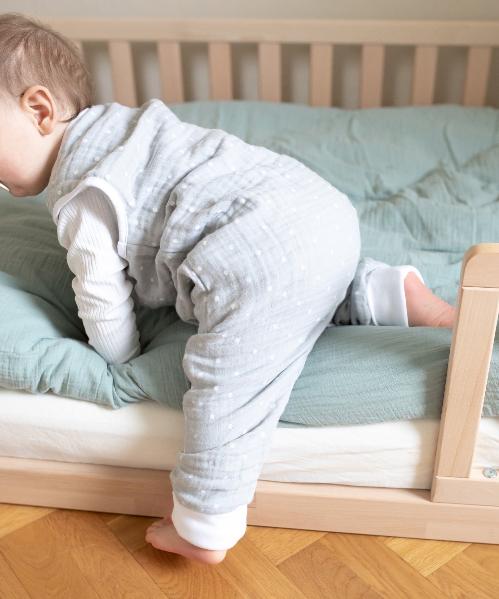 Maximale Beweglichkeit*Die Variante mit Beinen ist die perfekte Wahl für Kinder, die gerne mehr Beinfreiheit haben.|Baby mit Musselin Sommerschlafsack mit Beinen steigt aus Bodenbett.