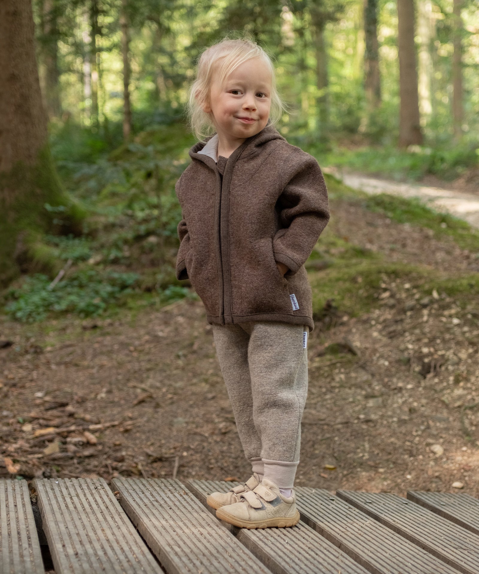 Kind mit Walkjacke und Walkhose steht im Wald.
