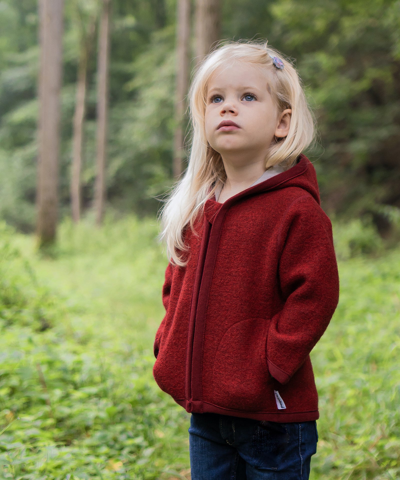 Mädchen mit roter Walkjacke steht im Wald.