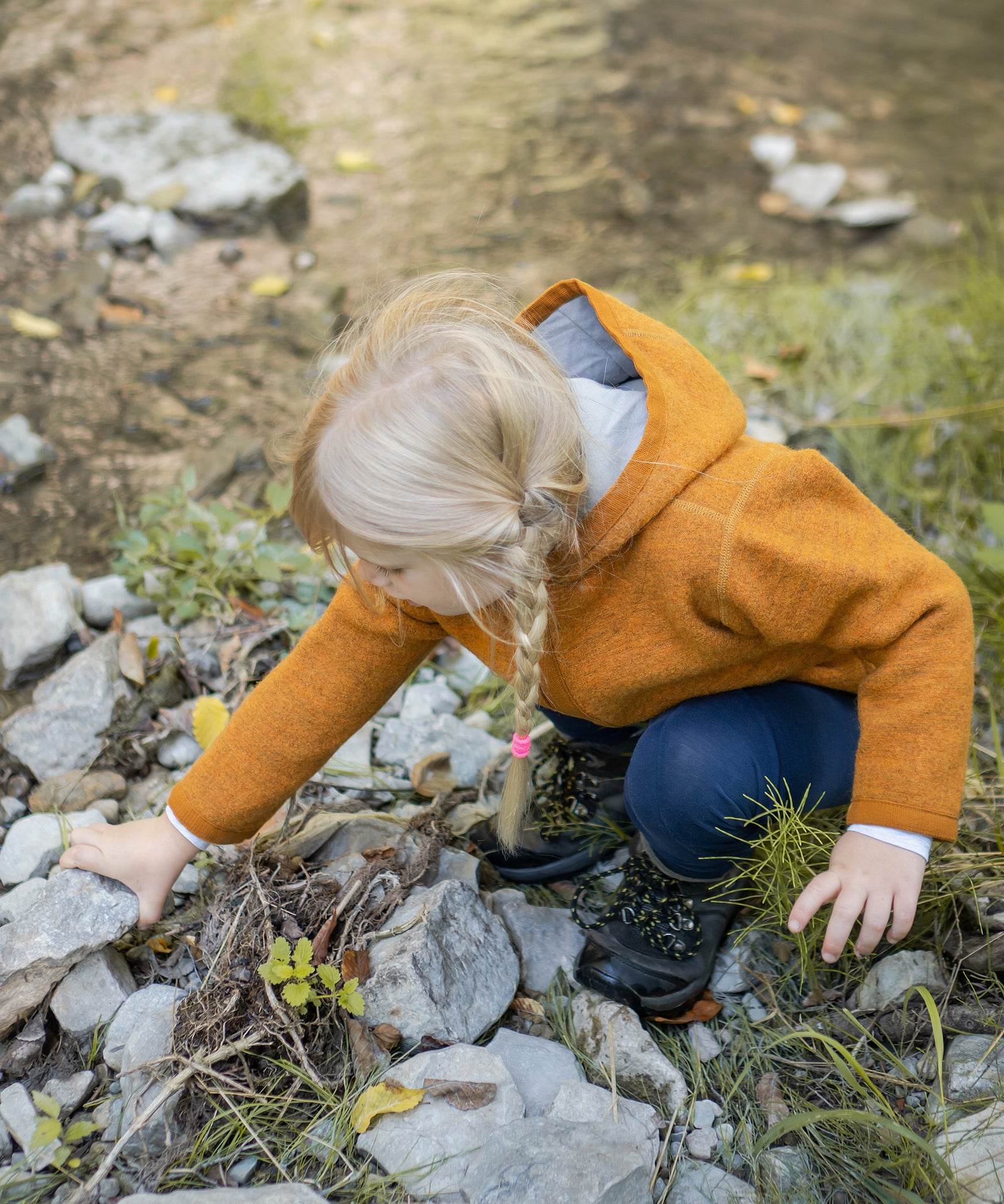 Natürlich wärmend & wetterfest*Der Walkstoff verfügt über sehr gute Wärmeeigenschaften und ist von Natur aus schmutz- und wasserabweisend.|Kind mit Walkjacke in safrangelb spielt mit Seinen am Bach.