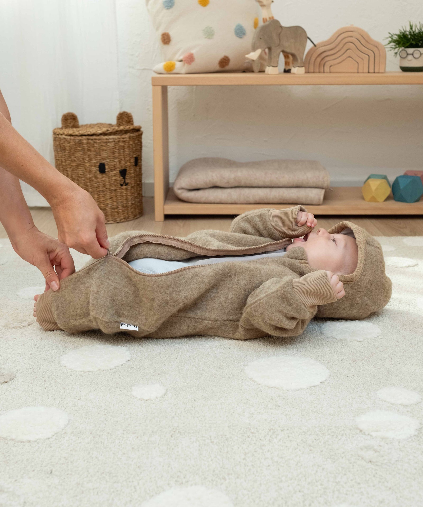 Leichtes An- und Ausziehen*Mit dem leicht asymmetrischen Reißverschluss lässt sich der Wollfleece-Overall schnell und unkompliziert an- und ausziehen.|Mutter zieht Baby Wollfleeceoverall an.
