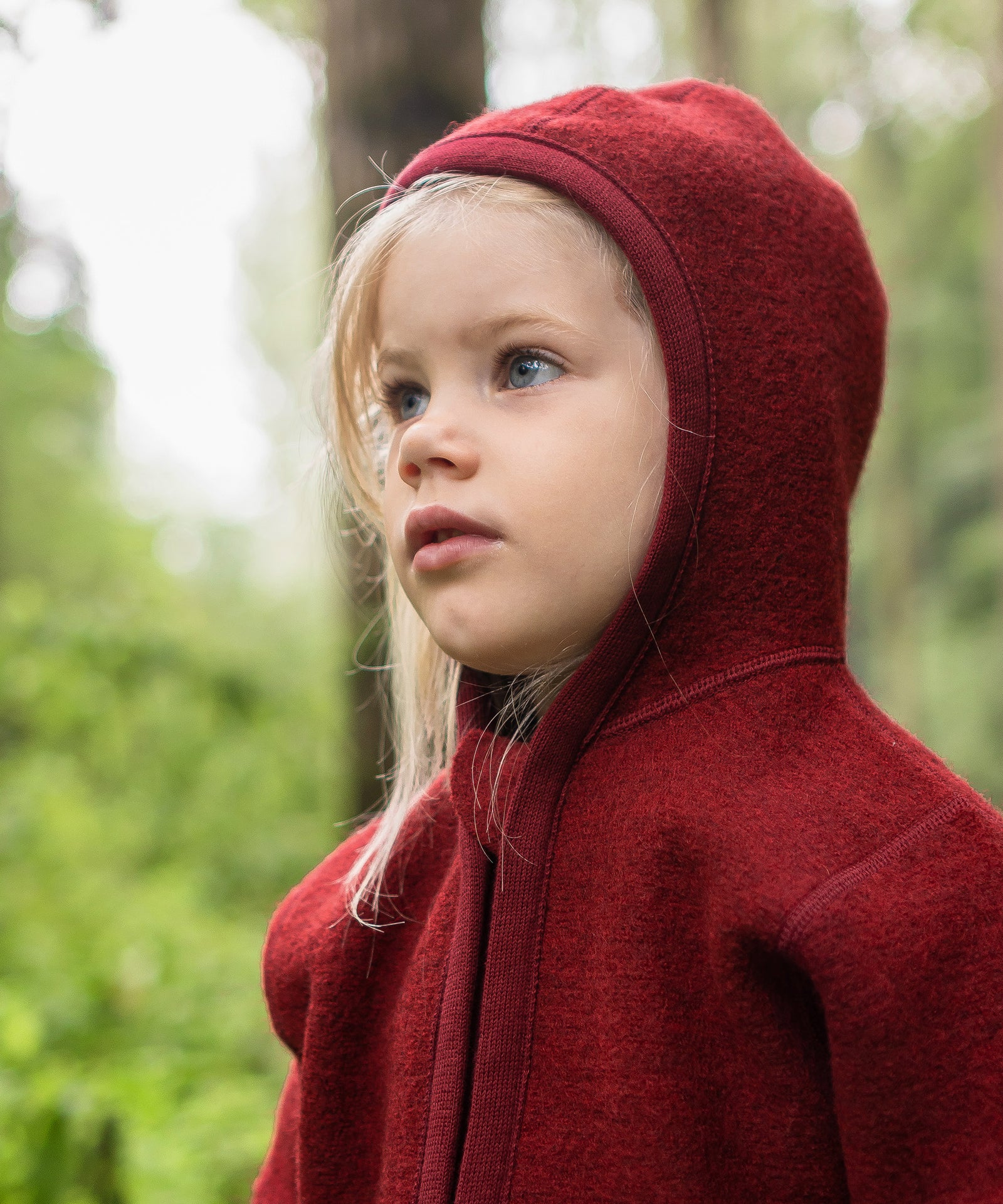 Nachhaltig & fair produziert*Die verwendete Schurwolle ist mulesingfrei und stammt aus artgerechter Tierhaltung.|Mädchen mit Walkjacke rot mit Kapuze auf dem Kopf.