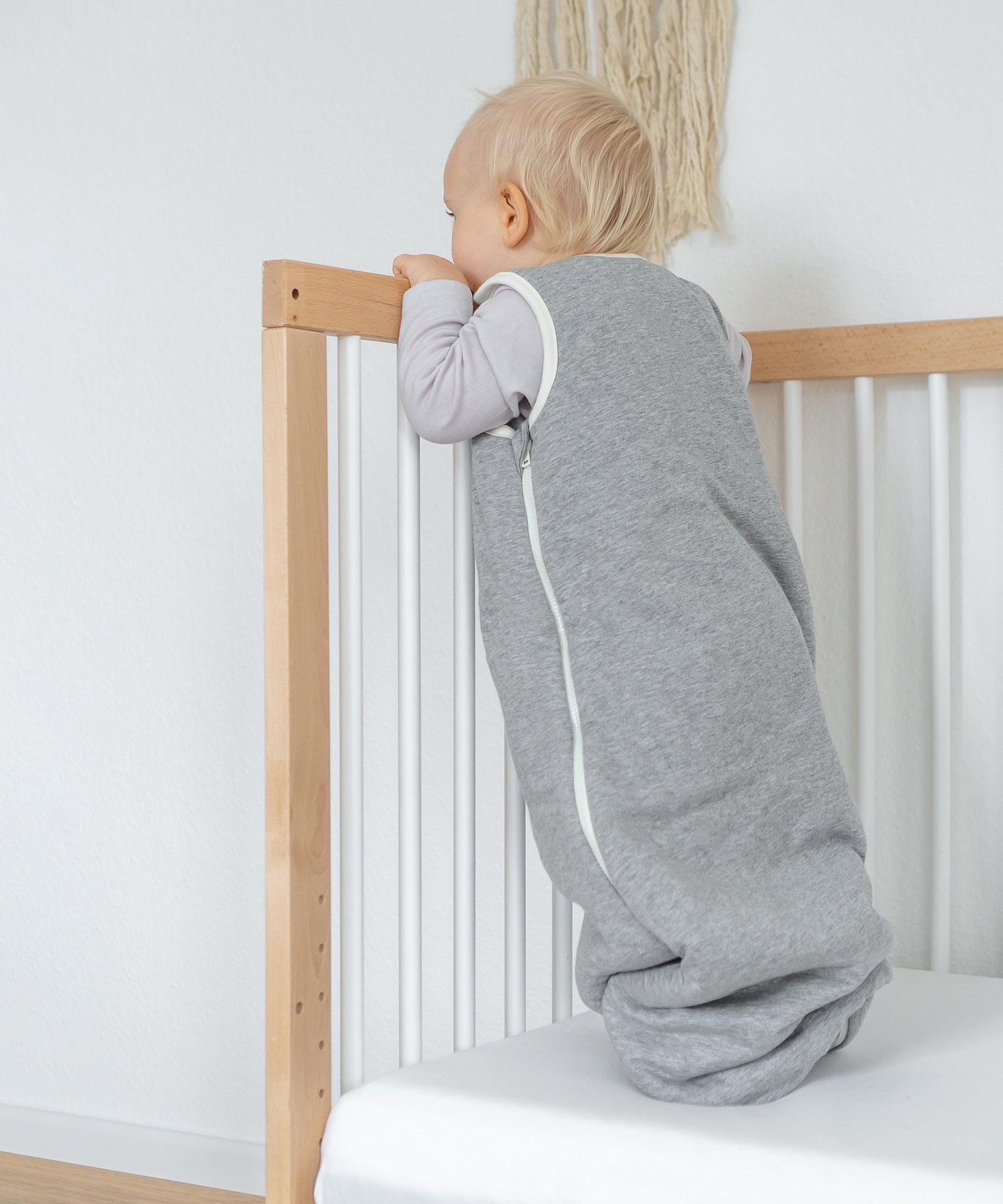 Baby in grauem Schlafsack stehend.