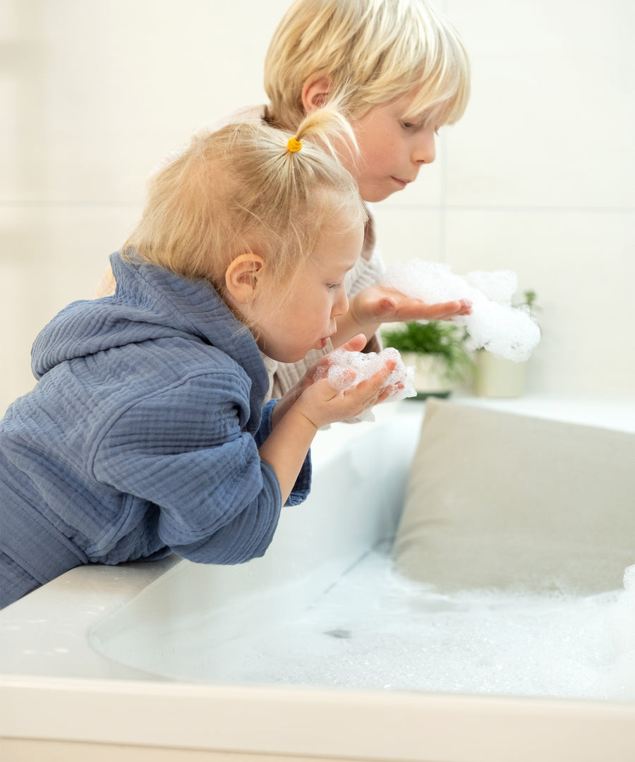 Kinder mit Bademantel aus Musselin für Kleinkinder spielen mit Schaum.