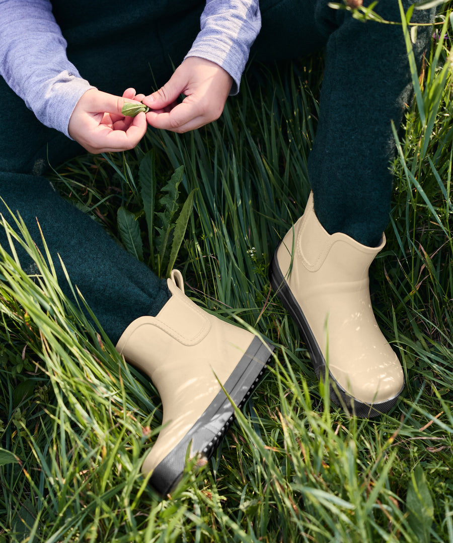 Mix & Match*Alle Farben sind auf unsere Outdoor-Bekleidung & Accessoires aus natürlicher Wolle abgestimmt und perfekt kombinierbar.| Kind trägt Walkhose in Waldgrün und Barfuß-Gummistiefel in Beige.