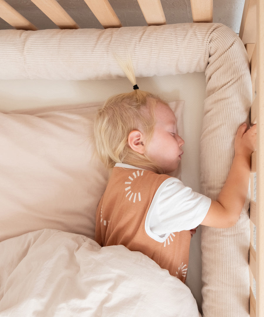 Kind schläft im Kinderbett, am Rand rundherum liegt die Bettschlange in Beige.
