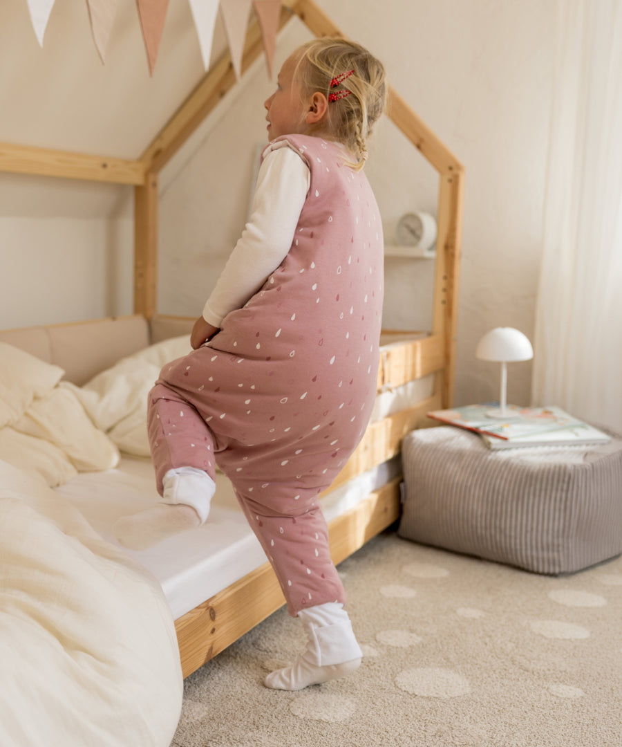 Bewegungsfreiheit für aktive Kinder*Der mit OEKO-TEX® Standard 100 zertifizierte Schlafsack ist ideal für Kinder, die bereits eigenständig krabbeln oder laufen.| Kind trägt den Winter-Schlafsack in Rosé Tropfen und steigt ins Hausbett.