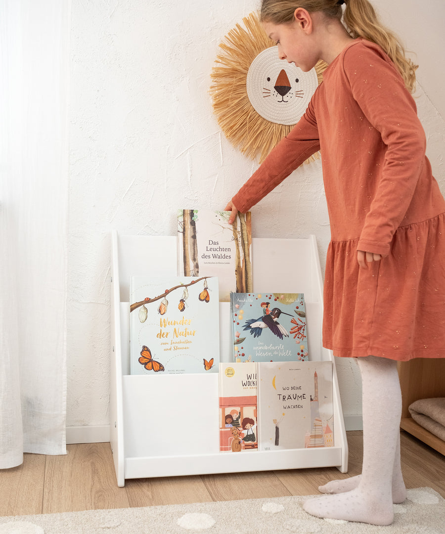 Fördert die Entwicklung*Das Bücherregal nach Montessori fördert die Selbstständigkeit deines Kindes und regt so die Kreativität an.|Kind stellt Buch in Bücherregal.