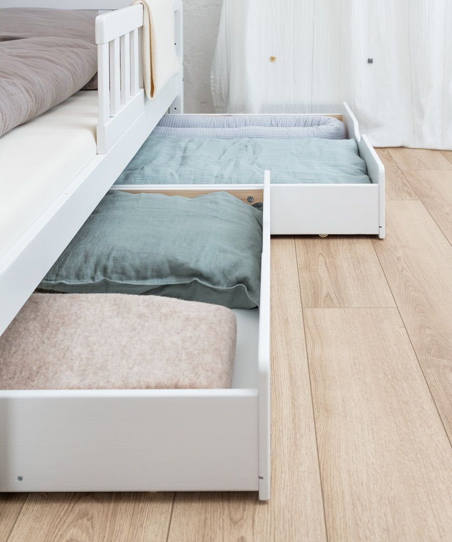 Extra Stauraum*Unsere optionalen Bettschubladen bieten zusätzlichen Stauraum für Groß und Klein.|Doppelschublade vom Hausbett Kiefer in weiß befüllt und leicht ausgezogen, Schubladen haben praktische Rollen.