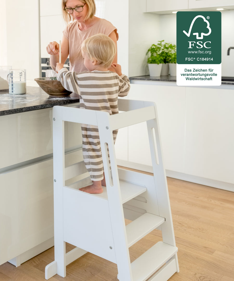 Kind steht im Lernturm und hilft beim Kochen in der Küche.