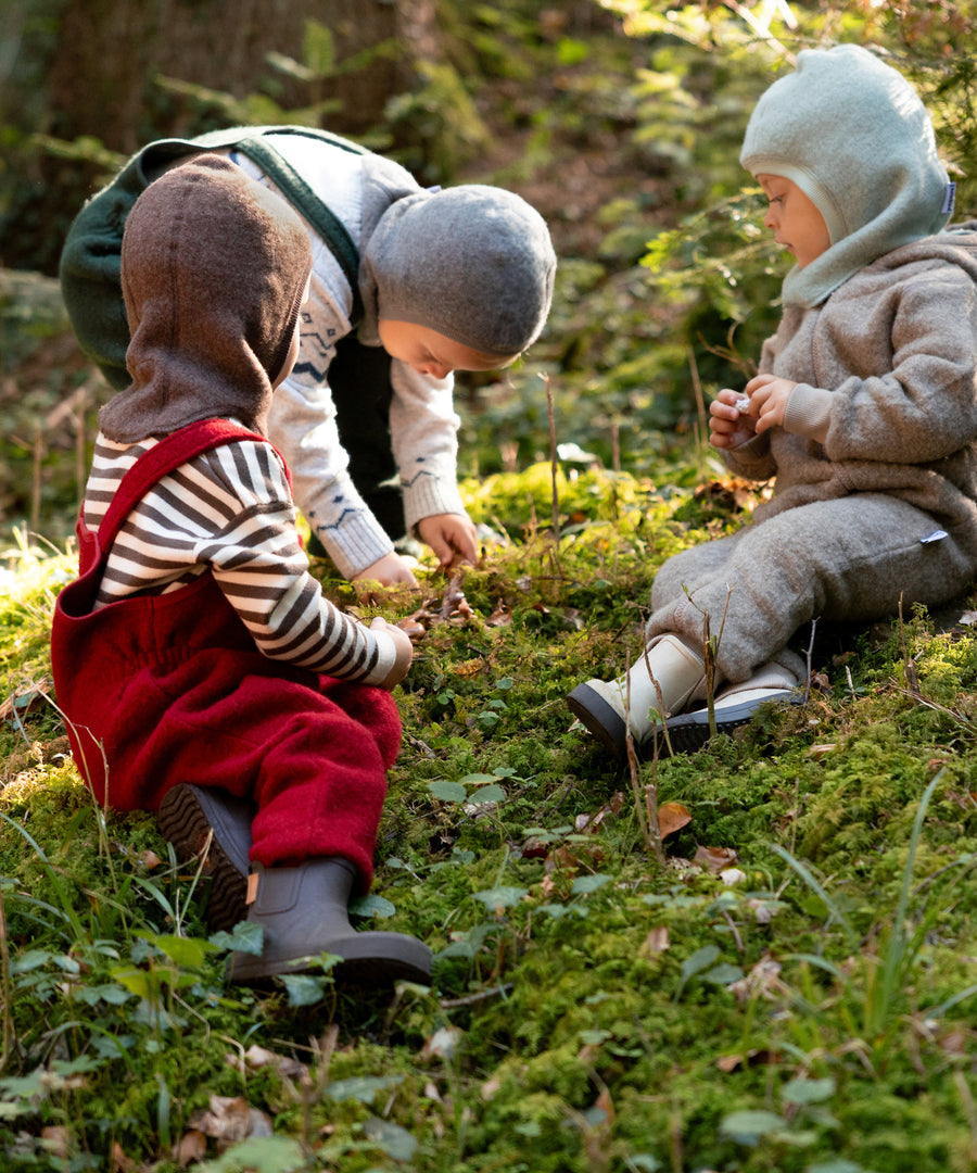 Fair produziert*Unsere Schlupfmütze wurde speziell für Babys & Kinder entworfen und wird in liebevoller Handarbeit in Europa hergestellt.|Kinder spielen draußen und tragen Schlupfmützen aus Wollfleece.