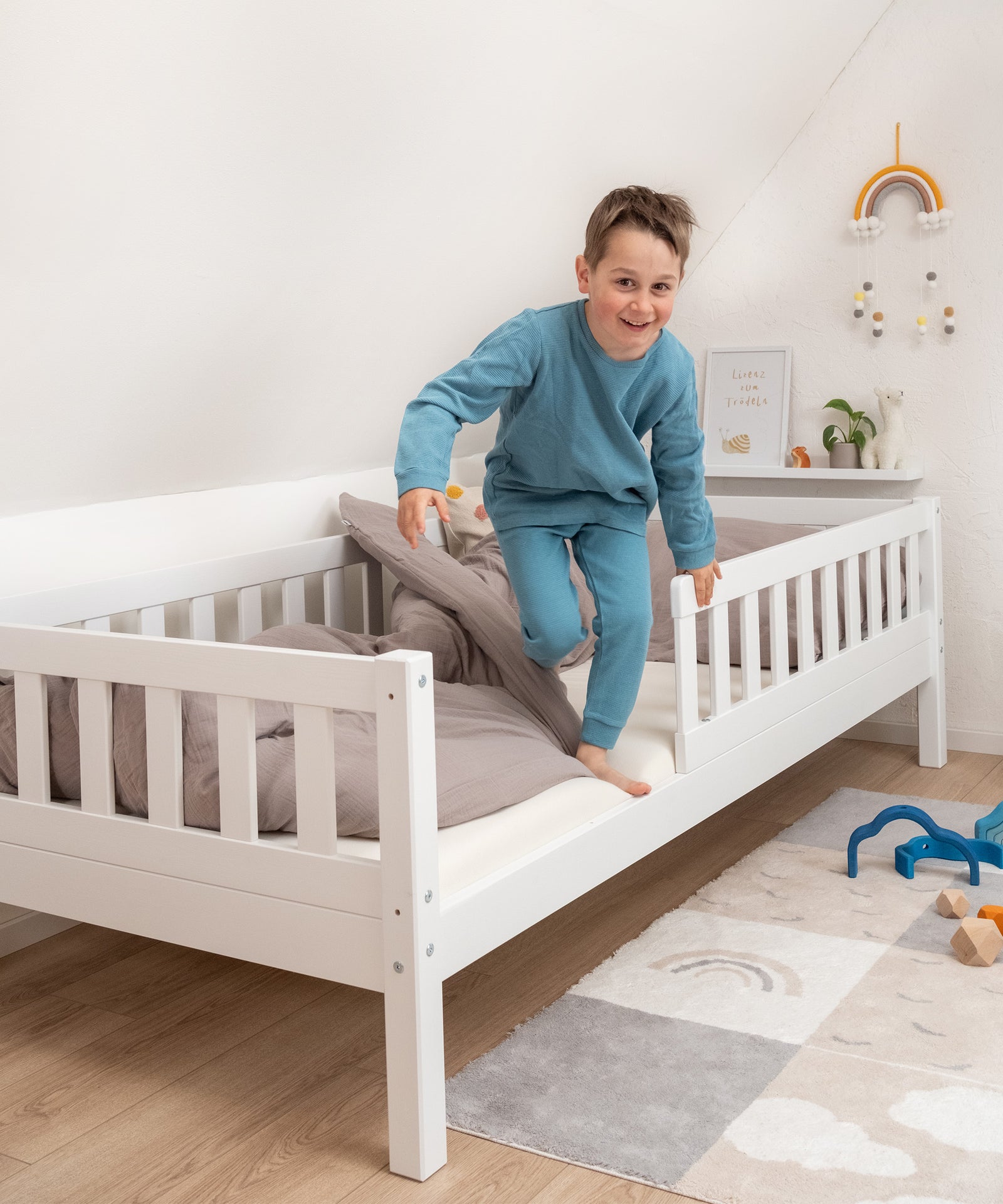 Junge steigt lachend aus Kinderbett Kiefer weiß.
