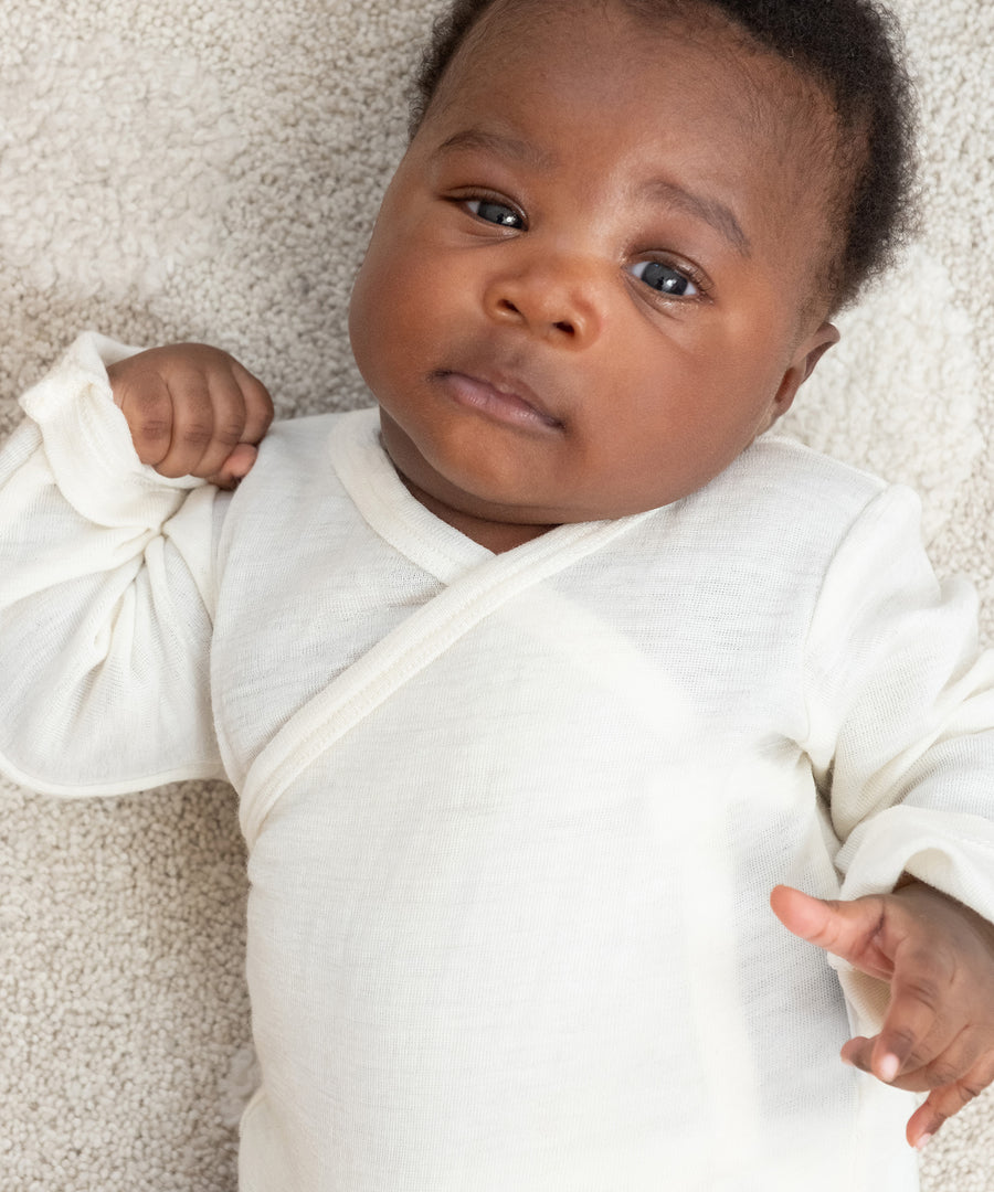Baby in Wickelbody liegt auf Teppich.