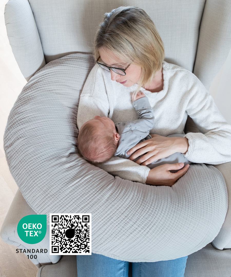 Frau mit Baby sitzt mit Stillkissen Musselin in Sessel, Stillkissen Oekotex zertifiziert..